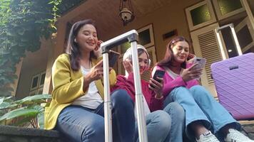 Three young women planning their trip. They are sitting with luggage, using their phones and enjoying time together, smiling and carefree. video