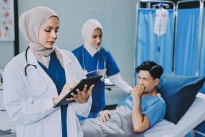 A woman in a hijab is holding a tablet while a man is in a hospital bed photo