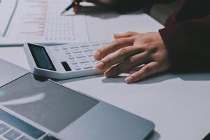 A person using a calculator on a desk with a laptop photo