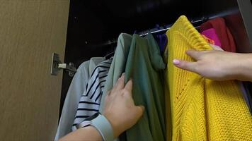 Selecting colorful clothes in a wardrobe, hands choose garments amidst a variety of textures and patterns video