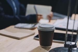 A coffee cup on a desk with a laptop and notebook photo