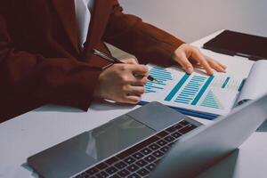 A person in a business suit is working on a laptop and a paper with graphs photo