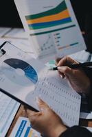 Businessman using a pen to write on a paper with graphs and charts photo