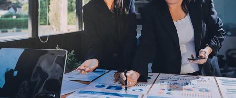 Two businesswomen working on a laptop in front of a table with papers and graphs photo