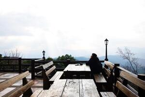 Beautiful sunset and silhouette woman sitting on wooden bench happy with valley mountain in the dark with cloud sky in Thailand photo
