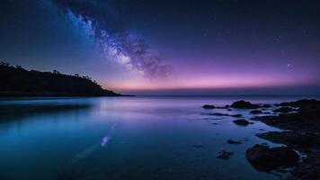 A serene nightscape featuring the Milky Way over calm waters and rocky shorelines. photo