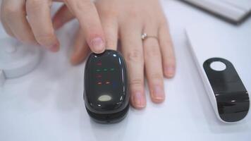 A close-up of a doctor measuring a patients pulse and heart rate using a pulse oximeter. The device is clipped onto the patients fingertip, with the doctors hand gently adjusting it to ensure video
