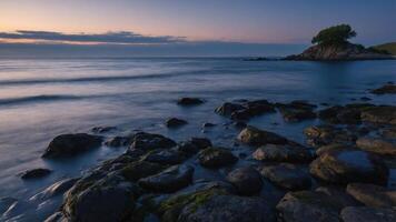 A tranquil coastal scene at sunset with rocks and a solitary tree on a small island. photo