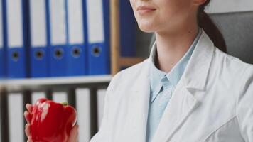 A dietitian in a white lab coat sits in a clinic, eyes closed, reflecting on nutrition plans. Colorful binders line the shelves, indicating a well-organized workspace focused on health. video
