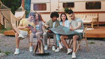 A diverse group of friends enjoys a relaxing summer day outdoors, gathered around a campfire while discussing their weekend camping plans. Checking the map video
