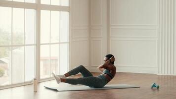 An African American woman performs a challenging workout at home, focusing on her core strength while surrounded by natural light from large windows. She embodies a healthy and athletic lifestyle. video