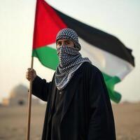 A man in a traditional palestinian outfit stands in the desert holding a palestinian flag photo