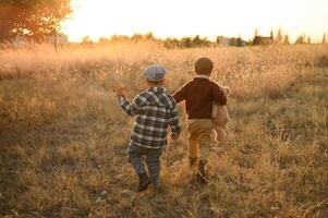 In a warm sunset glow, two young boys in old-fashioned outfits share a quiet moment in a field with an apple and a plush bear. photo