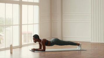 uma determinado africano americano mulher envolve dentro uma prancha exercício dentro de casa, exibindo dela atletismo e comprometimento para uma saudável estilo de vida. luz solar preenche a sala, realçando dela exercite-se atmosfera. video