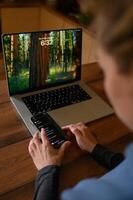 A person sits in front of a laptop, holding a phone showing a chat with ChatGPT on the screen. photo