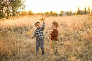 Bathed in golden light, two boys in classic vintage outfits play joyfully with a teddy bear, a small airplane, and a shiny apple in hand. photo