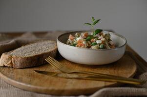 A creamy Olivier salad alongside rustic sourdough bread on a plate, styled in a food photography setting. photo