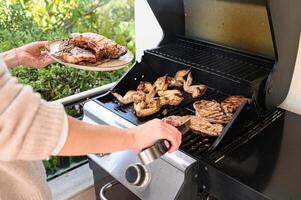 One hand grips metal tongs turning sizzling meat on the barbecue, the other balances a plate loaded with freshly grilled chicken and steak. photo
