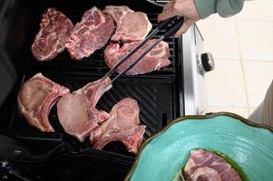 Hands arrange uncooked steaks on the smoking grill, with marinated mushrooms set aside, waiting their turn. photo