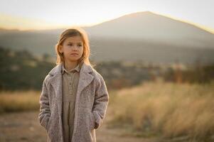 A dreamy portrait of a girl in a dusty pink coat, standing near an empty field under the afternoon light. photo