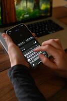 Close-up of hands using a smartphone with a ChatGPT chat open, while a laptop rests on a desk nearby. photo