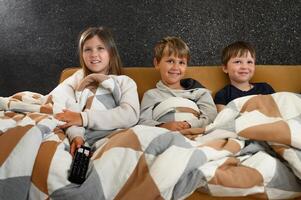 Children relaxed on a couch in front of a glowing screen, their faces animated with happiness and shock as they react to the program. photo
