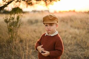 A young boy wearing a vintage cap holds a single olive in his hand, gazing at it with thoughtful curiosity in soft, nostalgic light. photo