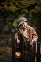 In the soft glow of dusk, a boy in retro attire grips a lantern, his face lit gently by its warm light on an old bridge. photo