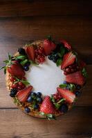 Top-down view of a golden honey cake with visible layers, topped with a generous handful of fresh berries and a light sugar dusting photo