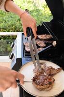A perfectly seared steak is being cut with a sharp knife, one hand gripping tongs to hold the meat in place. photo
