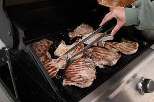 A close-up shot of juicy beef steaks sizzling on a charcoal grill as a pair of stainless steel tongs flips one over, smoke curling in the warm afternoon light. photo