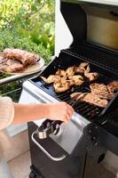 A close up of busy hands at the barbecue one turning meat with tongs, the other holding a dish piled high with cooked chicken and beef. photo