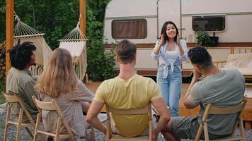A group of multiethnic friends relaxes outdoors, sharing laughter and stories while seated at a campsite, enjoying the summer vibes. Their playful interaction showcases friendship and fun. video