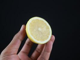 A man holds halves of a cut lemon in his hands. Exotic fruits in hands. Lemon close up, black background photo