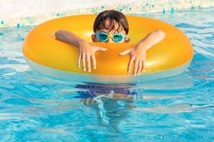 Child wearing swimming goggles relaxing in a pool with an inflatable ring on a sunny day photo