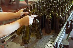 Wine bottling process, factory worker placing empty bottles on conveyor belt photo