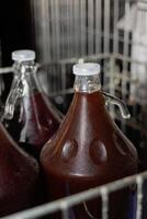Homemade red wine in large glass demijohns with handles, sealed with plastic caps. The bottles are stored in a metal crate, showing a stage of fermentation or aging. photo