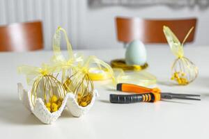 Close-up of handmade Easter eggs crafted from wire and ribbon, with tools on a white table photo