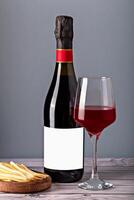 Wine bottle with blank label, glass of red wine and cheese slices on wooden board. Ideal for branding, advertising or culinary content. Glass red wine with bottle and sliced cheese on gray background photo