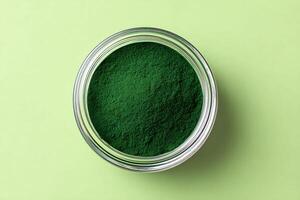 Green spirulina powder in a glass jar against a pastel green background highlighting its vibrant hue and nutritional benefits photo