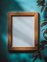 Blank frame for wall art mockup against a teal background with shadows and plant details creating a modern interior ambiance photo