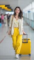 stylish traveler walks confidently through airport terminal, showcasing vibrant yellow outfit paired with light cardigan. She carries bright yellow suitcase, embodying cheerful and adventurous photo