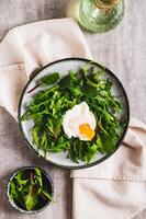 Leafy greens and poached egg on a plate on a table top and vertical view photo
