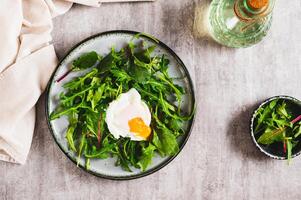 Poached egg in arugula and chard leaves on a plate on a table top view photo