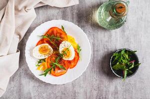 Light appetizer of tomatoes, boiled egg, cheese and arugula on a plate top view photo