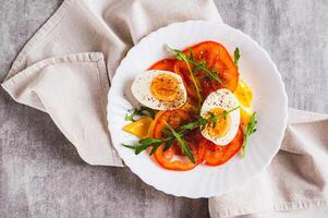 Close up of light appetizer of tomatoes, boiled egg, cheese and arugula on a plate top view photo