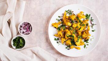 Baked spicy cauliflower with onions and parsley on a plate on the table top view web banner photo
