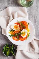 Tomato slices, egg, cheese and herbs on a plate on the table top and vertical view photo