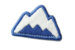 A blue and white embroidered patch features stylized mountain design, evoking sense of adventure and exploration. patch is outlined in blue, adding contrast and definition png