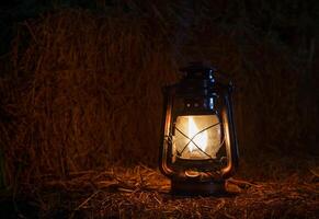 Antique kerosene lamp with light on hay bales in a barn at night photo